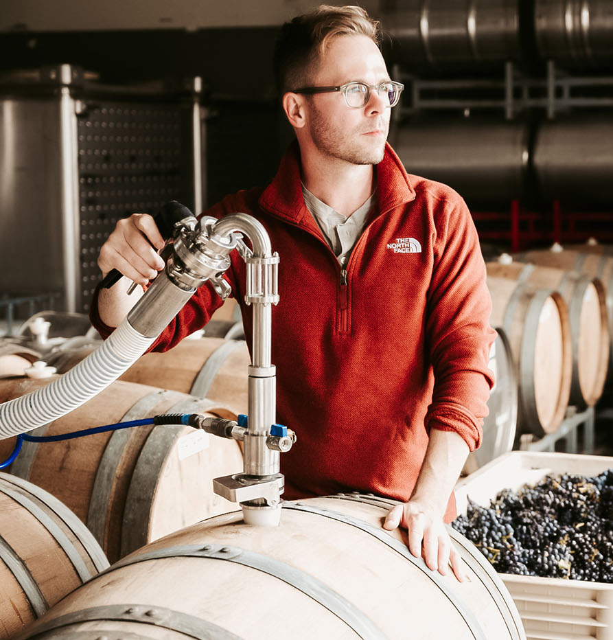Winemaker Chris Miller in the winery, filling a barrel with a bin of grapes behind him